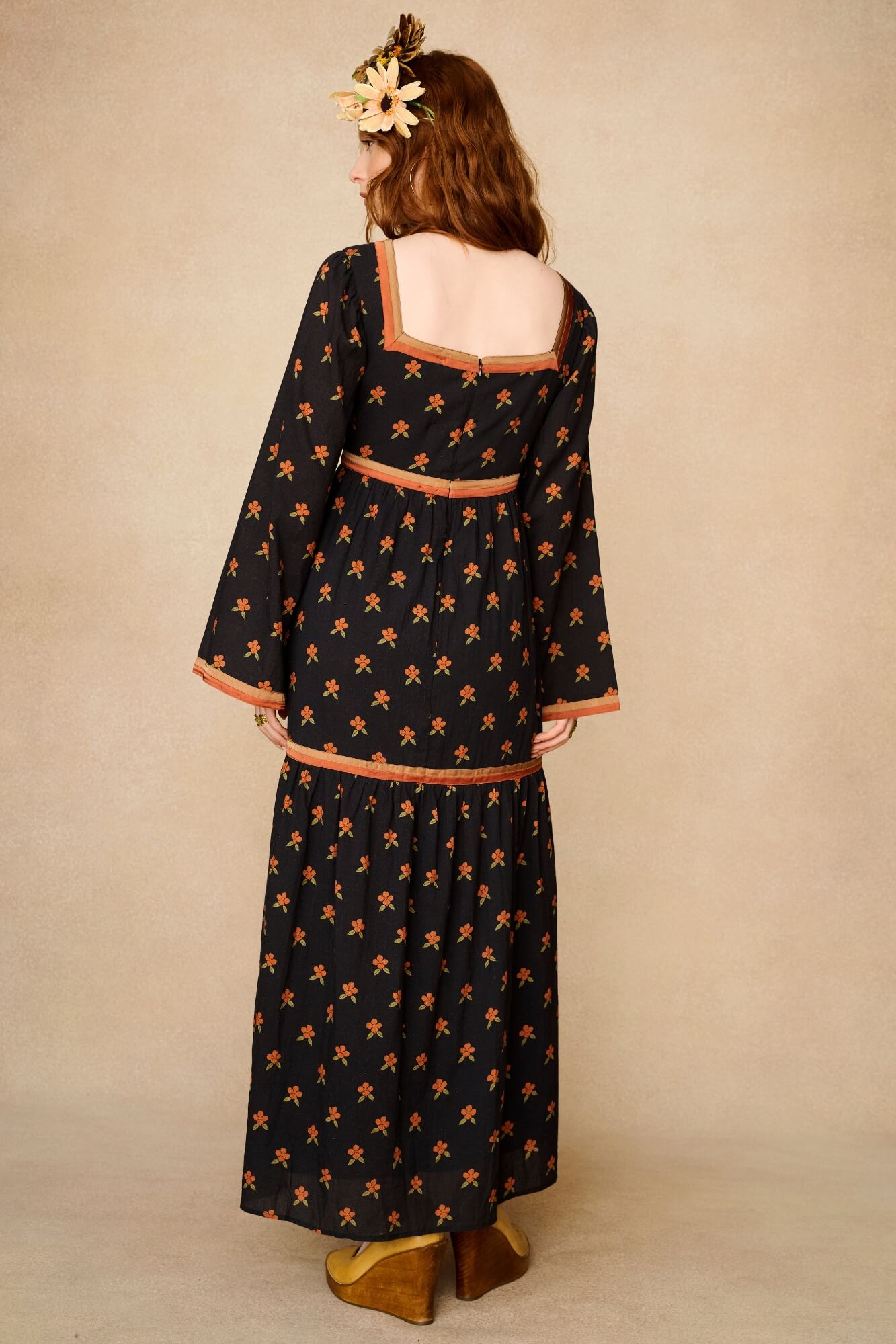 Woman wearing a black dress with orange patterns and a headpiece against a beige background