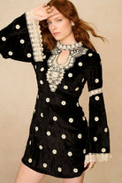 Woman wearing a black dress with white polka dots and lace details against a beige background