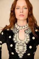 Woman wearing a black dress with intricate white lace details on a beige background