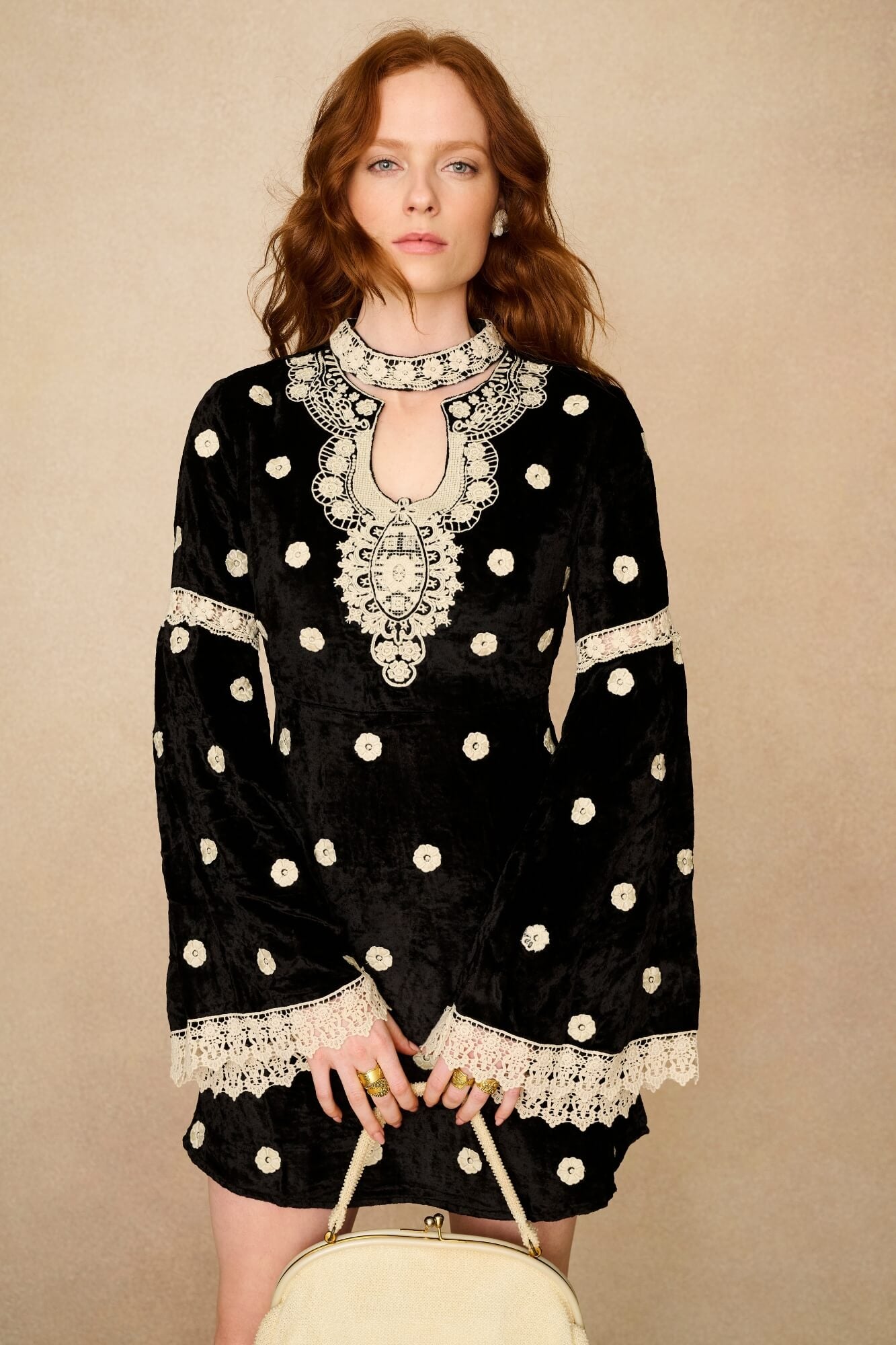 Woman wearing a black dress with white polka dots and lace details against a beige background