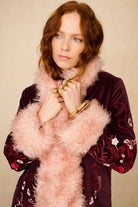 Woman wearing a burgundy embroidered dress with a pink fluffy scarf against a beige background - close up