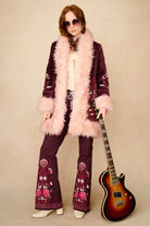 Person in a vintage-style outfit with floral patterns, holding a guitar against a beige background