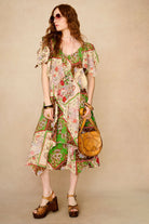 Woman wearing a colorful patterned dress holding a brown bag against a beige background  full body shot