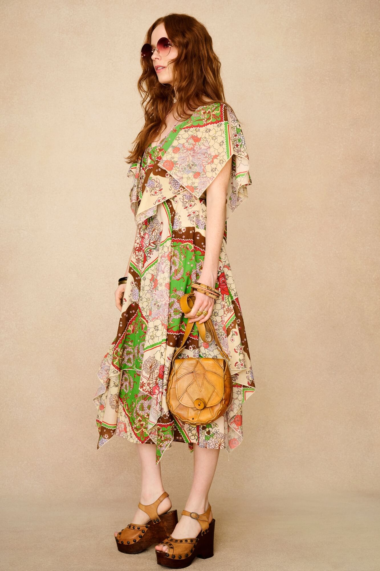 Woman wearing a colorful patterned dress holding a round handbag against a beige background - side shot