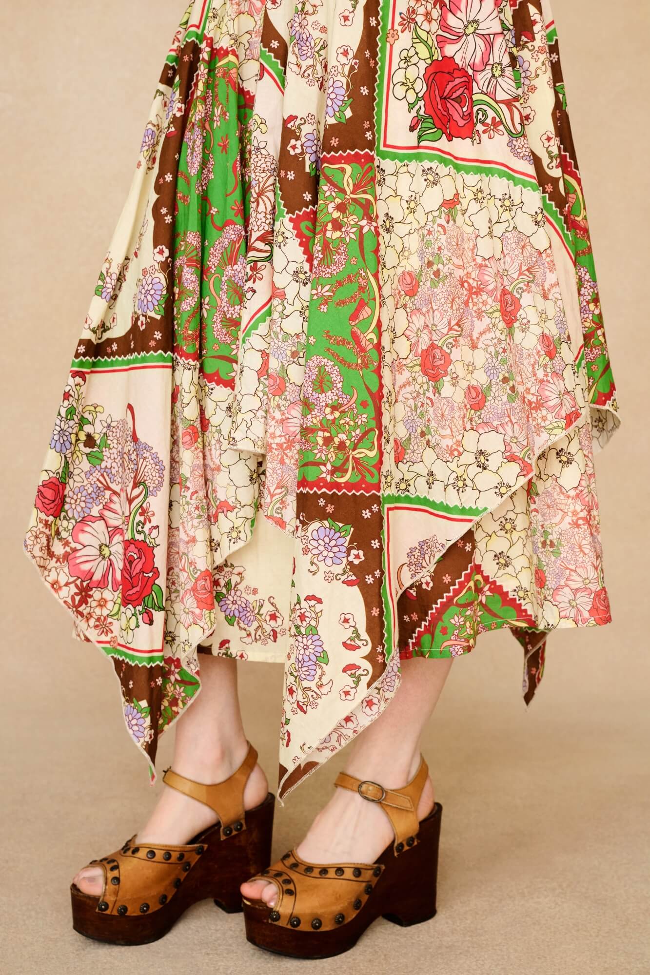 Person wearing a colorful patterned dress with wooden clogs on a beige background