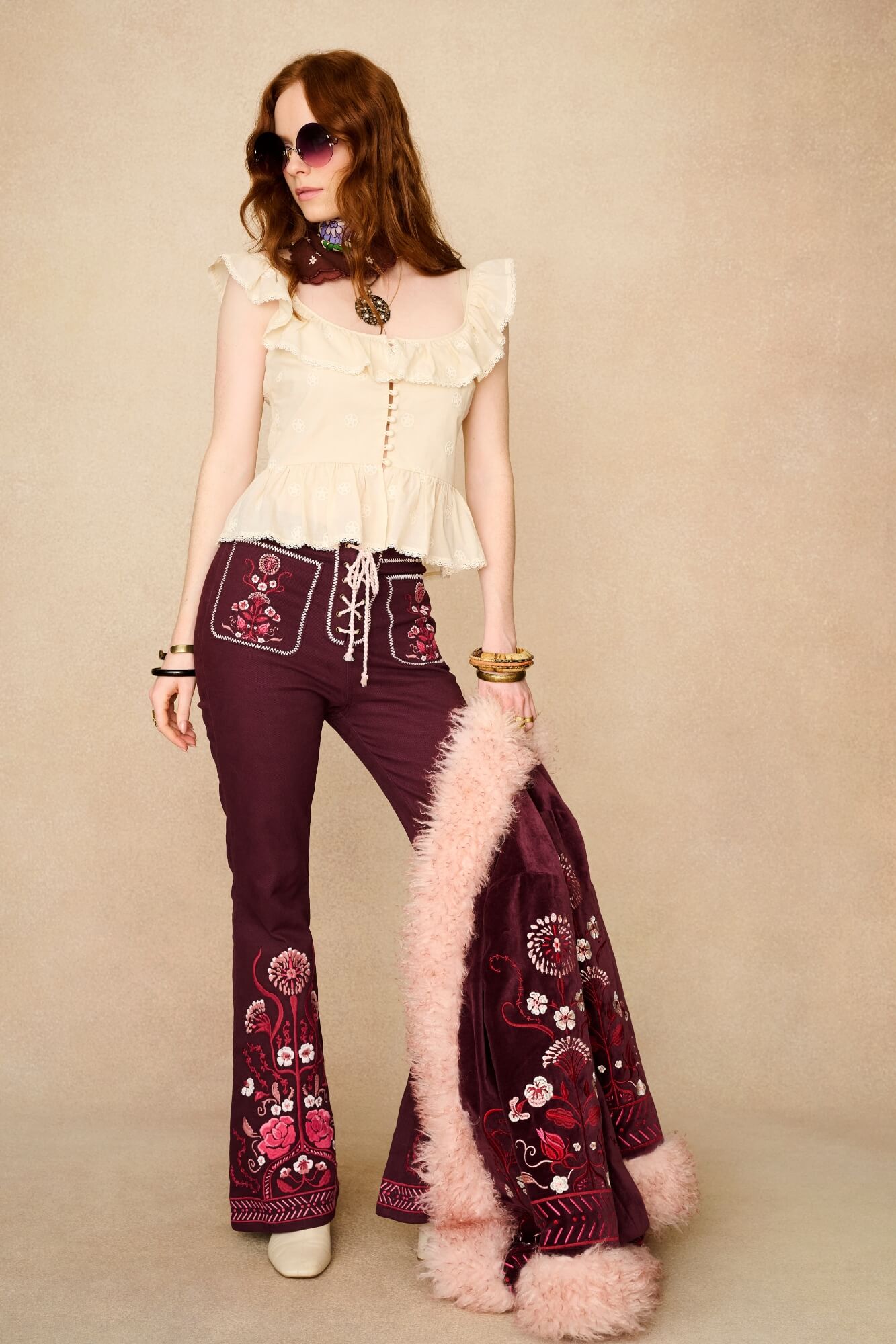 Woman wearing a white blouse and burgundy pants with floral embroidery against a beige background