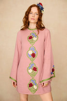 Woman wearing a pink dress with floral embroidery on a beige background