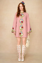 Model wearing a pink dress with floral embroidery and white lace-up boots on a beige background