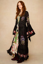 Woman wearing a black floral embroidered duster with a beige background