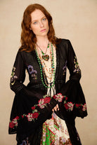 Woman wearing a black embroidered duster with floral patterns on a beige background