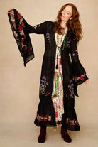 Woman wearing a black embroidered duster with floral patterns on a beige background