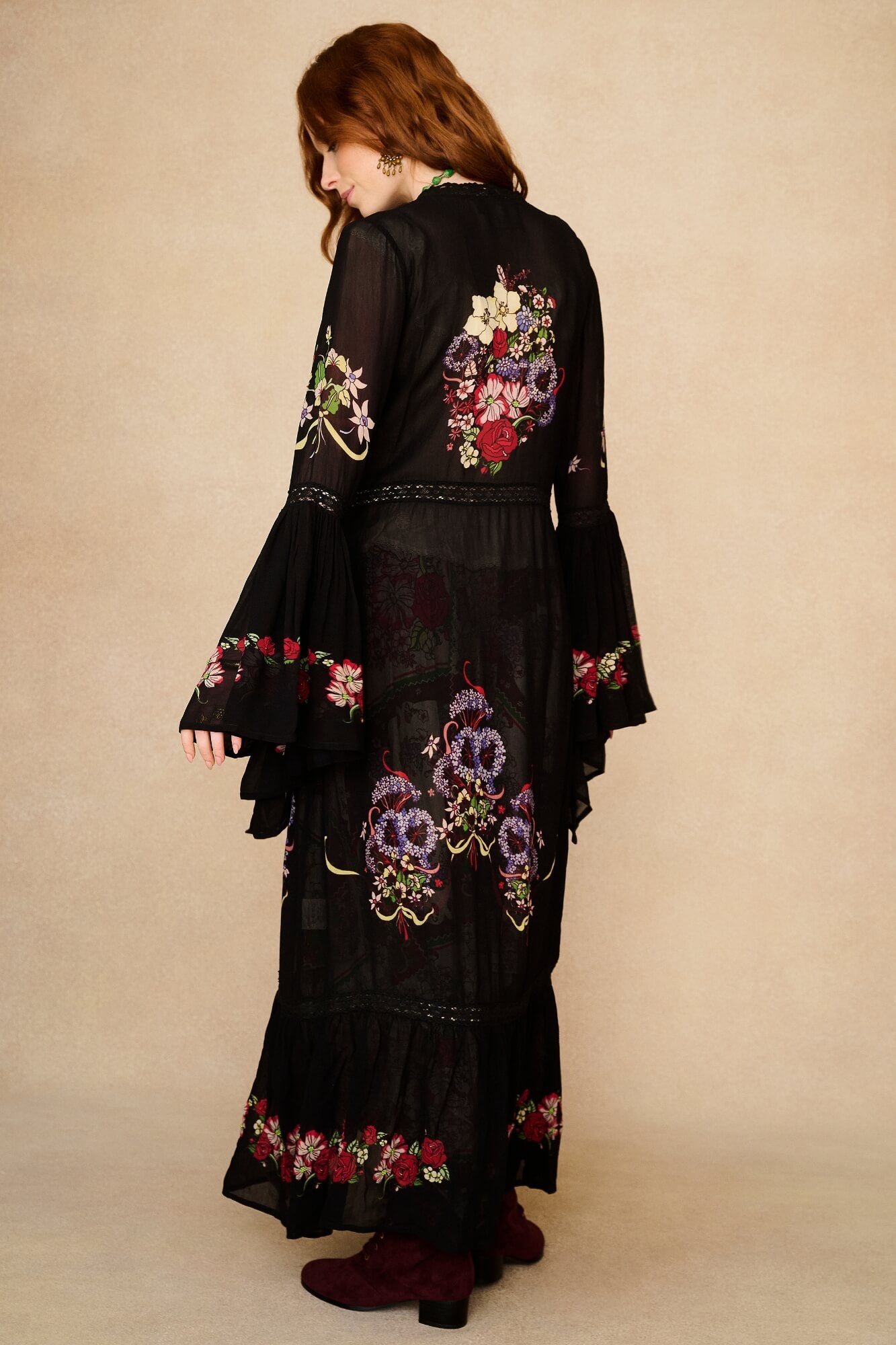 Woman wearing a black duster with floral embroidery against a beige background