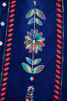 Close-up of a dark blue textile featuring colorful embroidered floral motifs and red leafy border details.