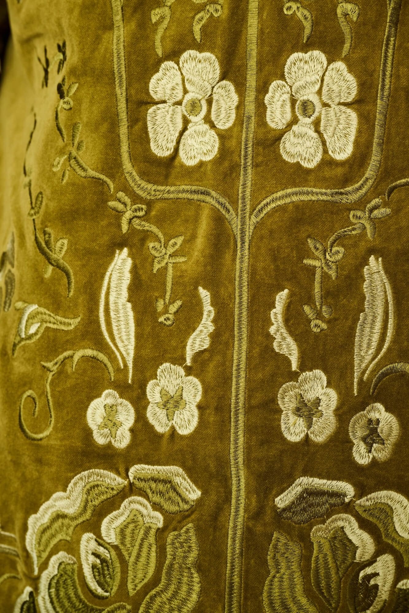 Close-up of an olive green embroidered textile with cream floral and vine motifs.