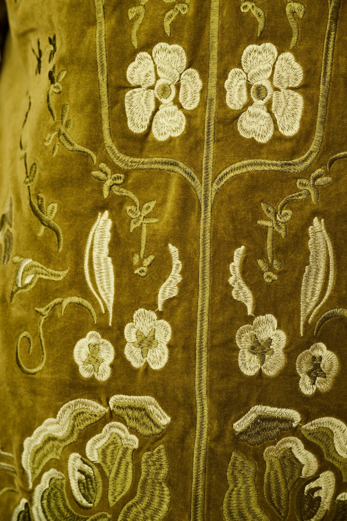Close-up of an olive green embroidered textile with cream floral and vine motifs.