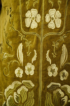 Close-up of an olive green embroidered textile with cream floral and vine motifs.