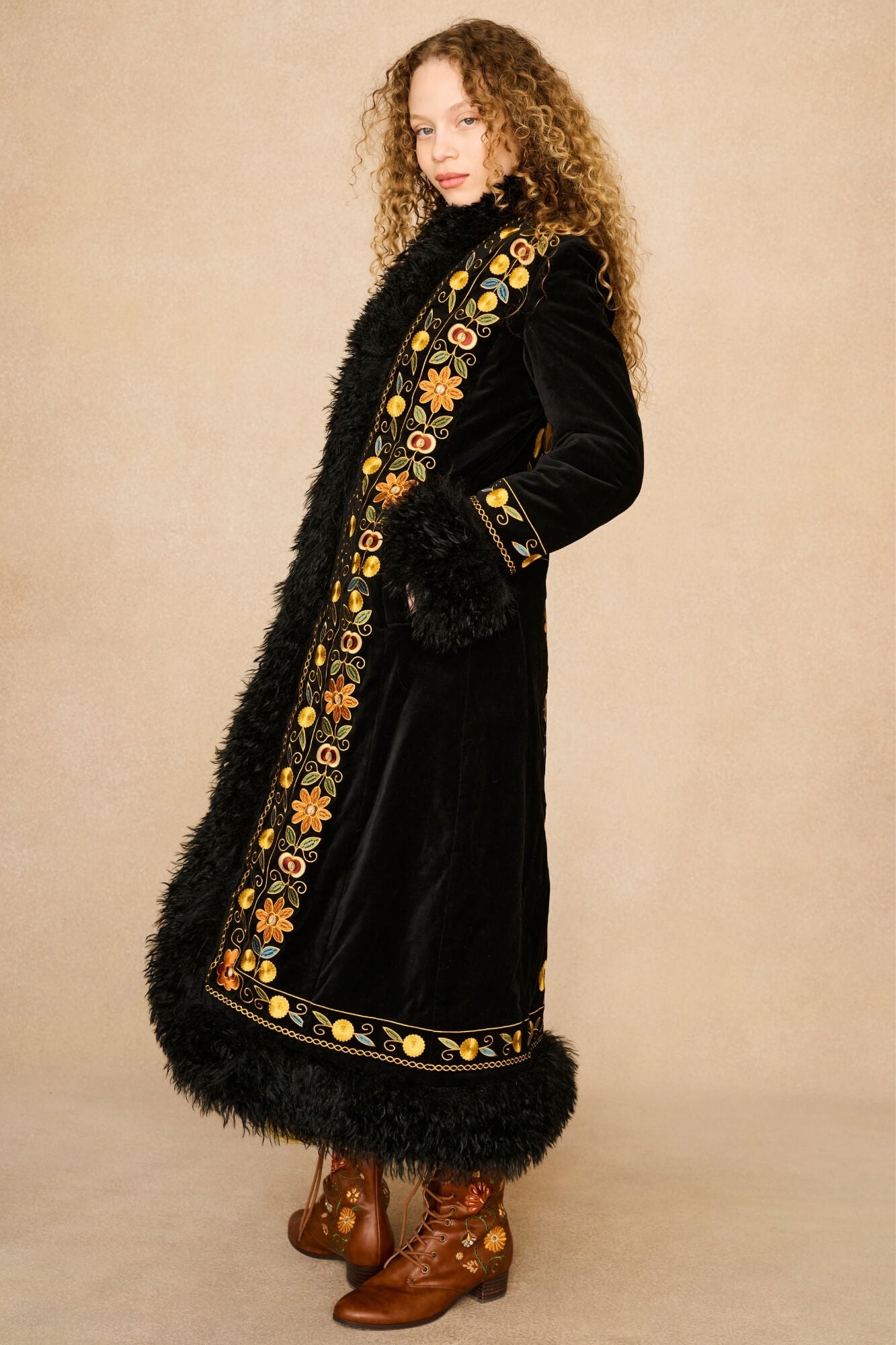 Model wearing long black Penny Lane coat by The Hippie Shake, with faux-fur trip and floral embroidery - side on view