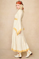Model wearing 70s cream long sleeve maxi dress with lace-up Penny Lane boots by The Hippie Shake, side view