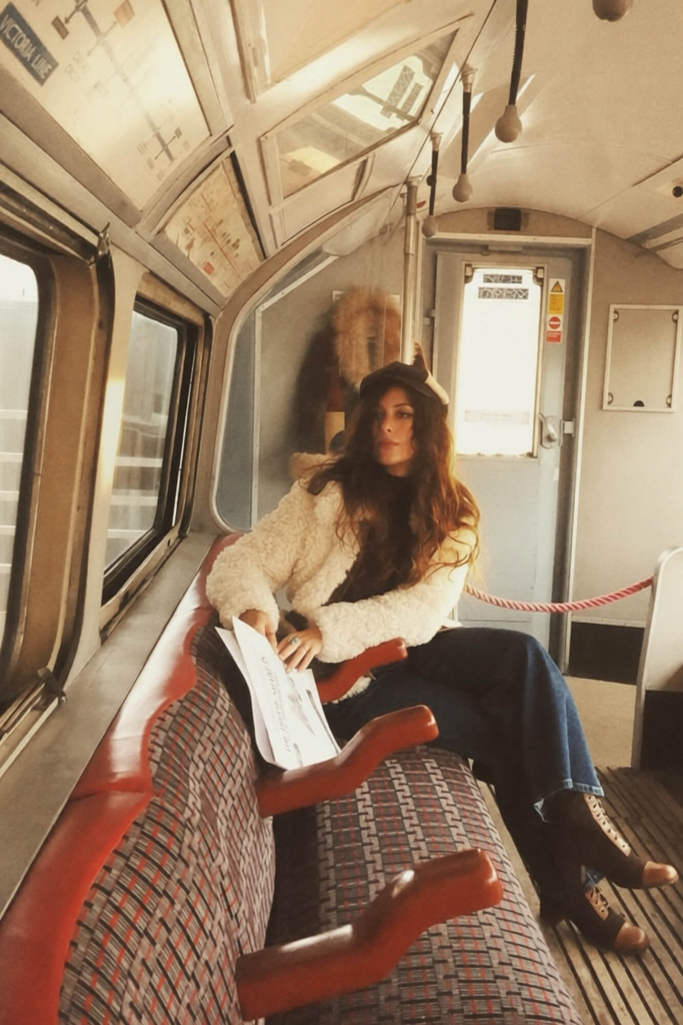 A woman inside a London tube train wearing a shaggy cream 70s jacket paired with denim flares and boots.